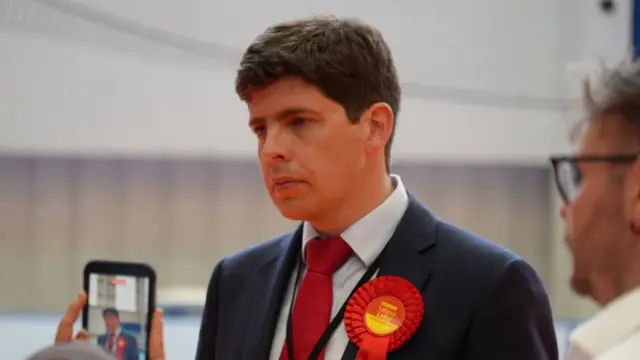 Huw Thomas is wearing a suit with a red lapel attached to it.