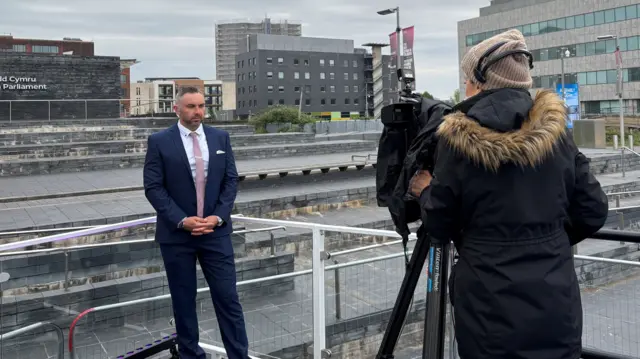 Tomos Morgan in front of the Senedd being filmed