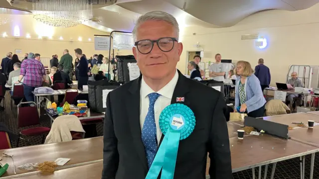 A photo of Andrew Rosindell with a big Reform ribbon