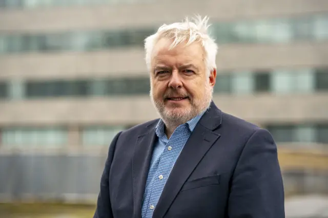 carwyn Jones in navy blazer and blue and white checked shirt and grey hair and beard