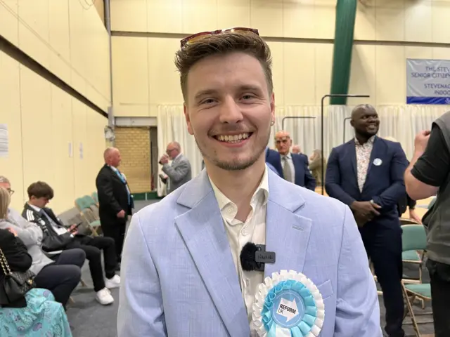Liam Morrell Phillips wears a Reform UK rosette and smiles at the camera