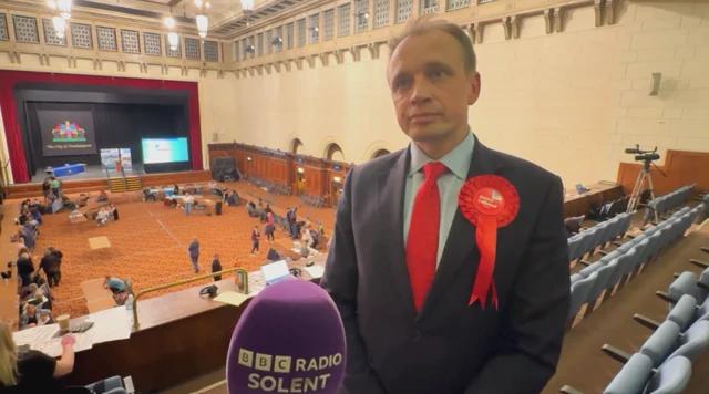 A man wearing a suit and tie and a Labour badge looking to the side of the camera.
