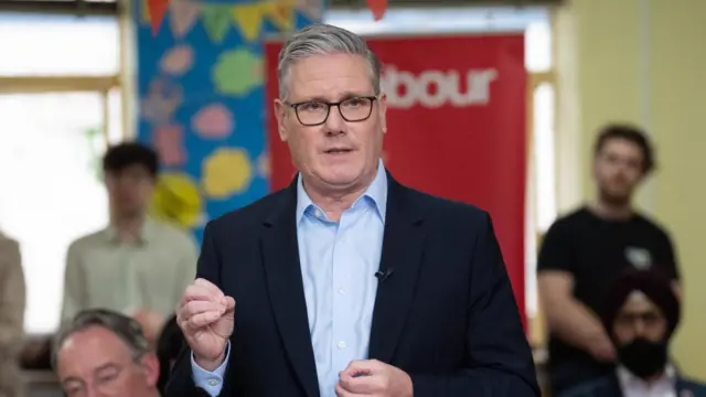 Keir Starmer stands in front of a Labour banner as he addresses a room full of people