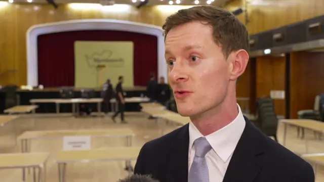 A man in a suit and tie being interviewed at an election count