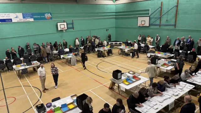 A leisure centre where an election count is being held. People sits at desks and chairs counting votes.