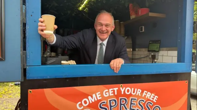Sir Ed Davey with a coffee in his hand leaning out of a hatch in a coffee van