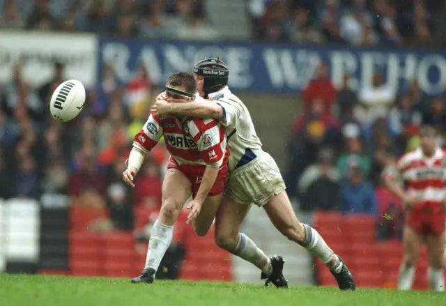 Martin Dermott of Wigan gets the ball away despite the efforts of Bernard Dwyer of St Helens