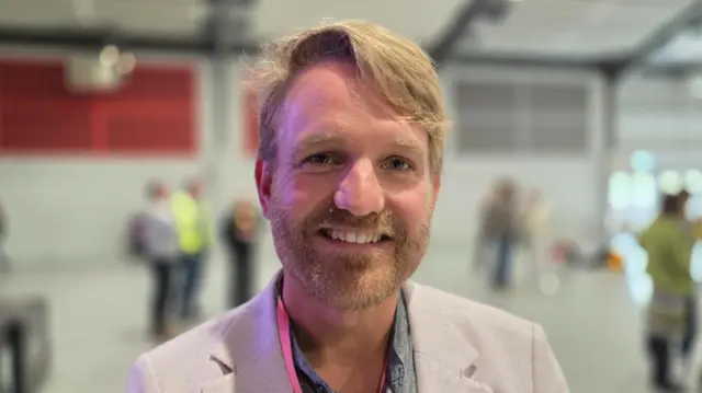 A man with blond hair and beard smiles at the camera