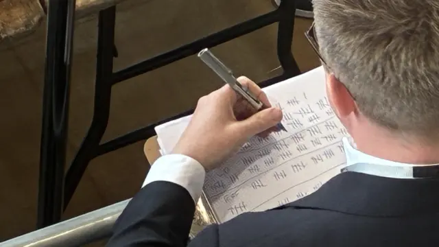 A photo taken above a man who is taking tallies on a piece of paper with a pen.