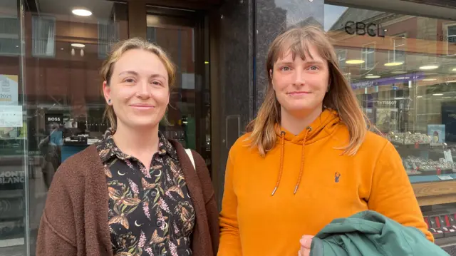 Charlotte and Bobbie pictured outside a jewellers, wearing a brown cardigan and black patterned shirt and an orange hoodie respectively