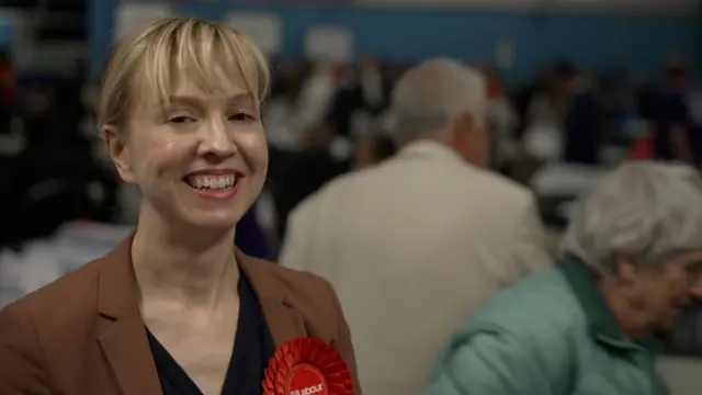 Woman with blond hair and red rosette smiling