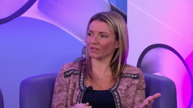 Francesca O'Brien is sat in a chair in front of a microphone wearing a red cardigan and a blue top.