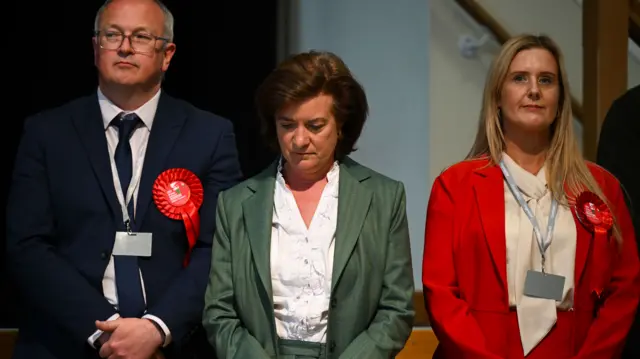 Eluned Morgan is wearing a green blazer and is looking down at the floor.