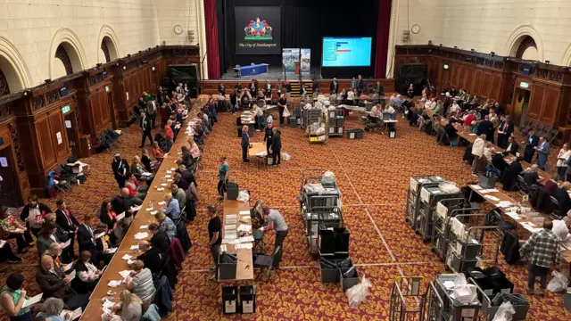 People gathered around a hall leaning over tables of paper.