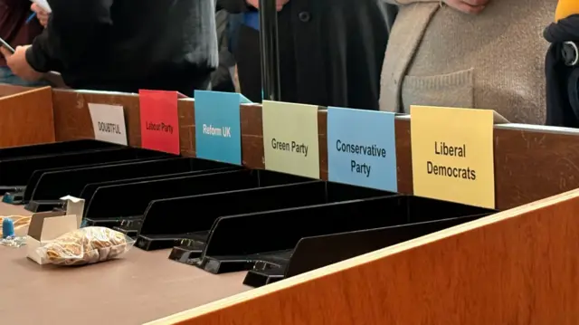 A selection of political party signs above empty black trays on a long table