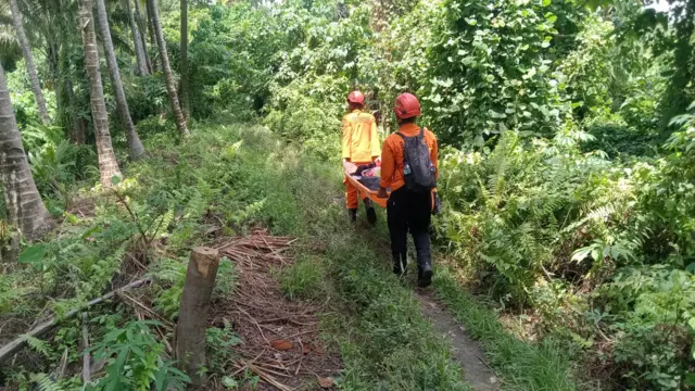 Two people in orange jumpsuits and helmets hike up a dirt track