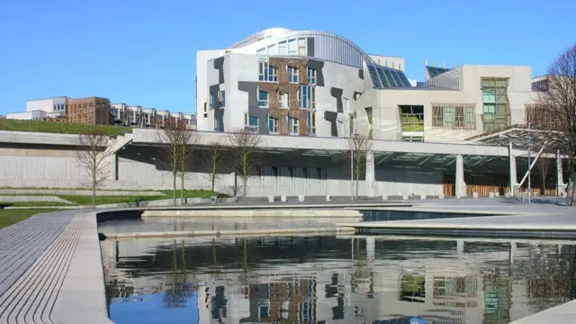 Scottish Parliament Building in Edinburgh, Scotland. A large structure with windows and a man-made water feature in front.
