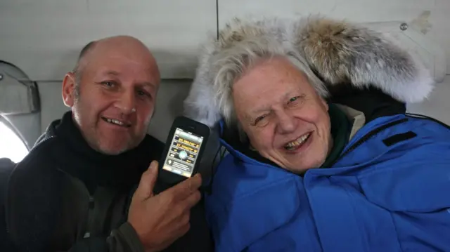 Gavin Thurston on the left holds an iPhone next to David Attenborough, who's wearing a polar jacket in the North Pole