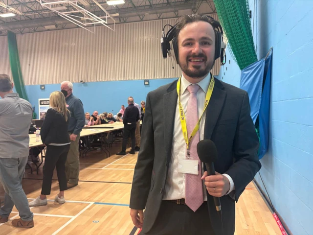 Edward Rowe with a microphone at the election count in Cheltenham