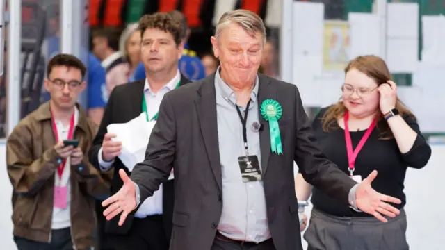 A man is smiling with his hands wide open, and people are behind him following him