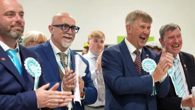 Newly elected Reform UK councillors (left to right) Bradley Thompson, Mark Webster, Peter Harris and Jeff Bray celebrate during the 2026 Essex County Council election at Clacton Leisure Centre