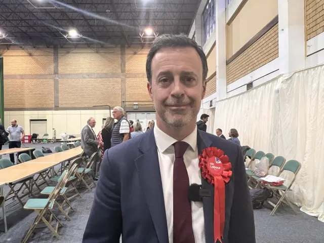 A man wearing a red Labour rosette in a large hall