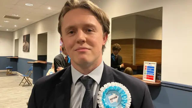 A young man in a suit wearing a blue and white rosette
