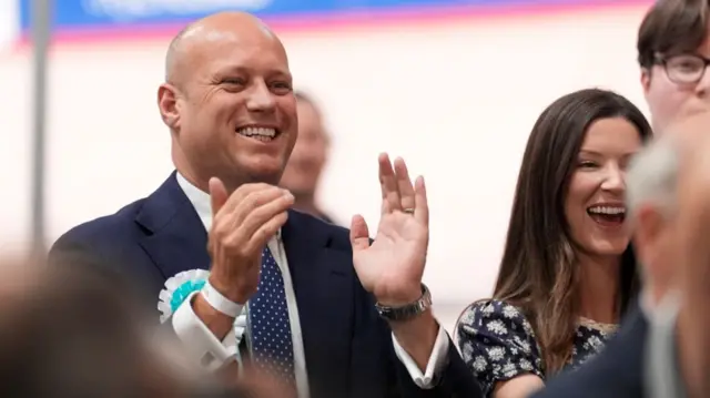 A man is clapping while wearing a blue lapel.