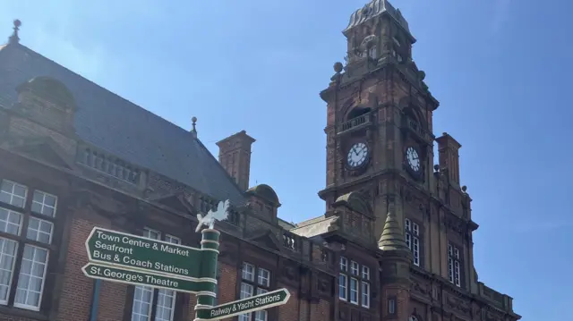 A red brick town hall building with a street sign post in the foreground