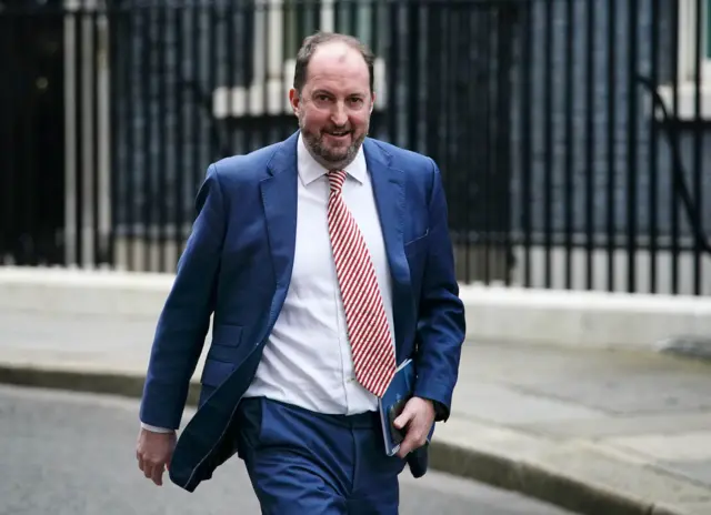 Guto Harri walks down Downing Street carrying a notebook.