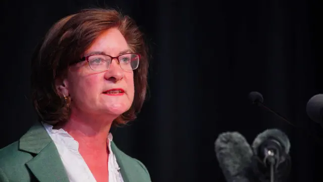 Baroness Eluned Morgan announces her resignation, she is wearing a white shirt, sage green suit and has brown hair