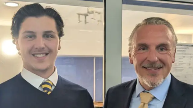 Jay Bartoli and Lewis Bartoli stand side-by-side and smile at the camera. On the left, Jay Bartoli has short black hair and is wearing a blue jumper and yellow striped tie. Lewis Bartoli is wearing a blue blazer and shirt, with a yellow tie. He has short greying hair and facial hair.