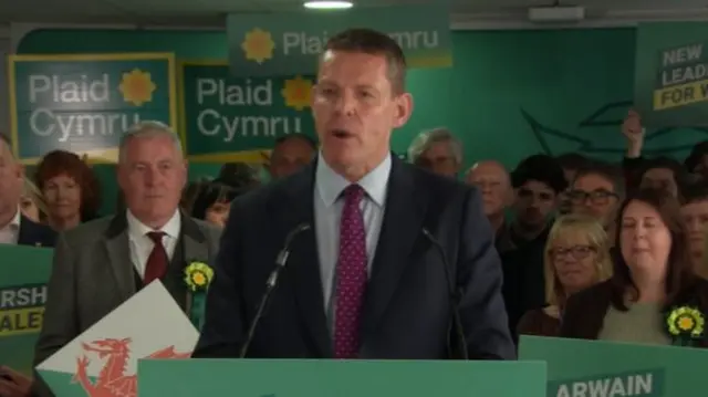 Rhun ap Iorwerth standing in front of a crowd of people holding Plaid Cymru placards