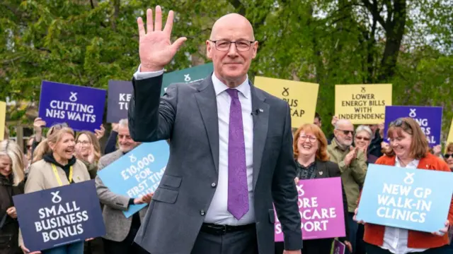 John Swinney waves on the campaign trail with supporters holding placards