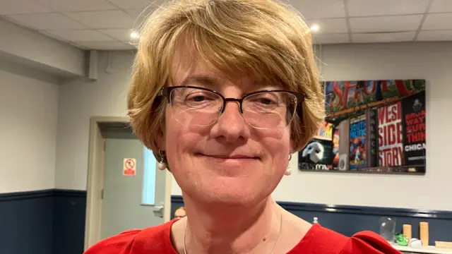A woman with short blonde hair and a red dress smiles at the camera