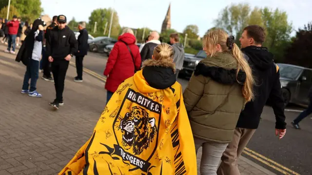 A Hull City fan walking to the ground draped in a flag