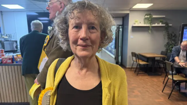 Phillipa Gray stood in a cafe wearing a yellow rosette and smiling at the camera.