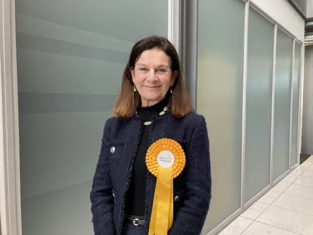A smiling Bridget Smith stares at the camera. She wears a Liberal Democrat rosette.