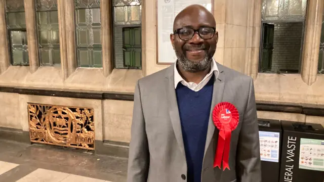 A man wearing a Labour badge smiling into the camera