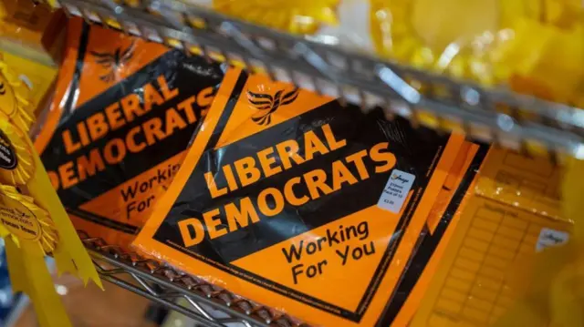 An orange placard saying 'LIBERAL DEMOCRATS, WORKING FOR YOU'.