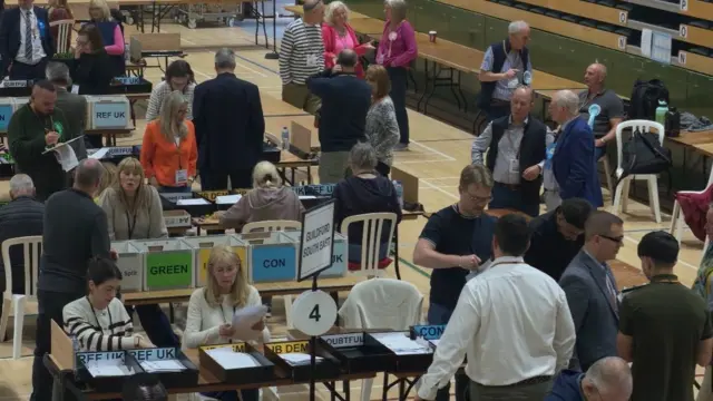 Dozens of people counting votes in a hall.