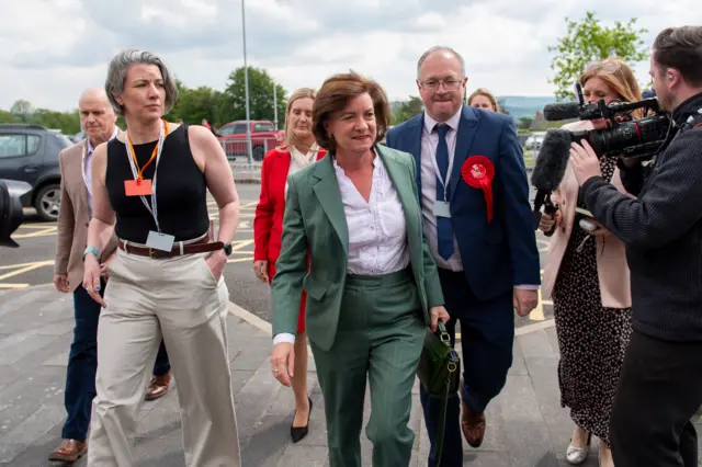 Eluned Morgan walking wearing green suit and white shirt flanked by people
