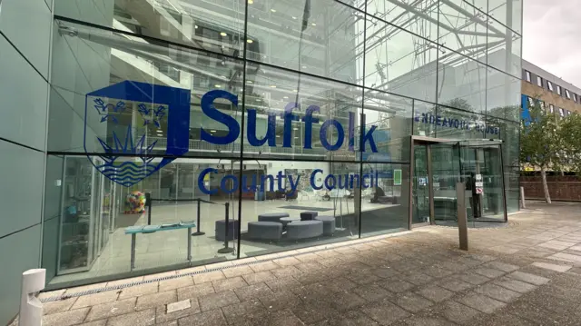 A view of the Suffolk County Council headquarters. It is a glass building with the name of the county council painting on the glass.