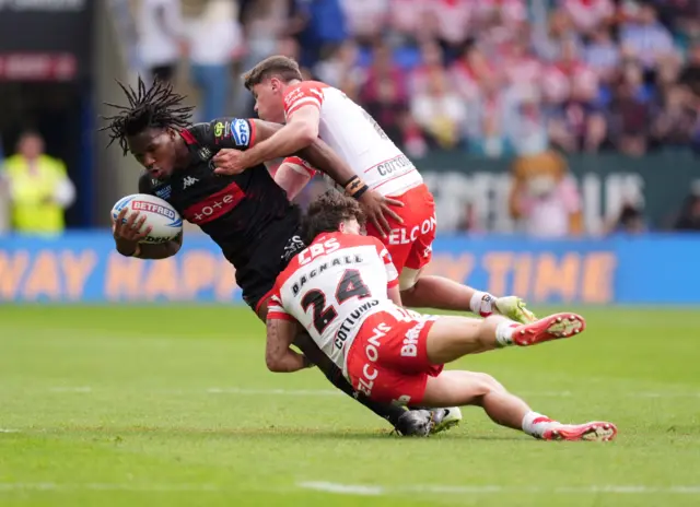 Wigan Warriors' Junior Nsemba is tackled by St Helens' Jack Welsby and Owen Dagnall