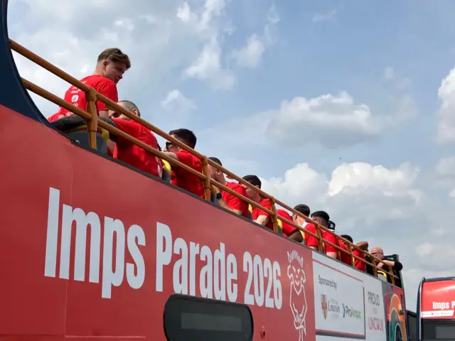 The writing on the bus says Imps Parade 2026. The players can be seen on the top behind the railings.