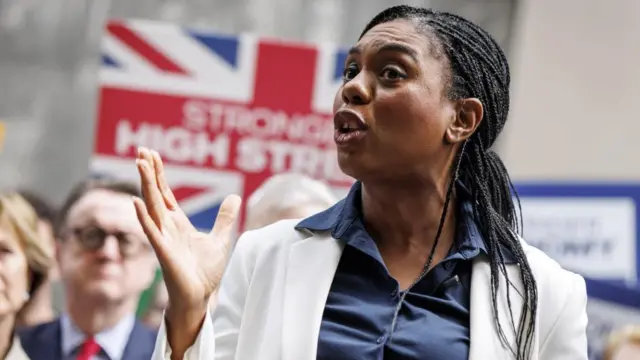Kemi Badenoch gestures in a speech with a union flag in the background