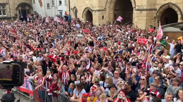 A wide shot showing hundreds of people outside the arches of the Cathedral
