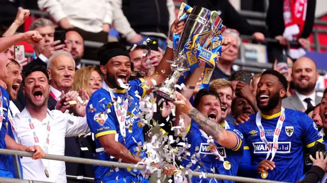 AFC Wimbledon players lift the League Two play-off final trophy at Wembley after beating Walsall in May 2025