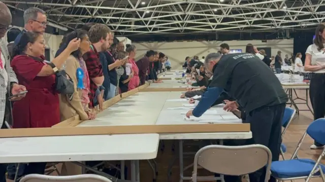 People standing round tables in a leisure centre where votes are being counted