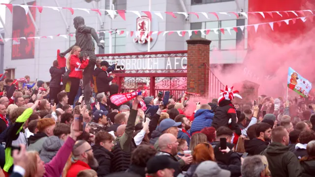 Huge crowds of fans outside Middlesbrough's Riverside Stadium with red smoke from flares and red and white bunting and flags